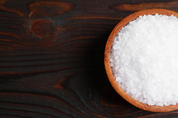 Bowl with natural sea salt on wooden table, top view. Space for text