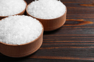 Fototapeta na wymiar Bowls with natural sea salt on wooden table, closeup. Space for text