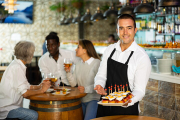 Fototapeta na wymiar View on the Latino young man holding pinchos at a bar with diverse group in the background