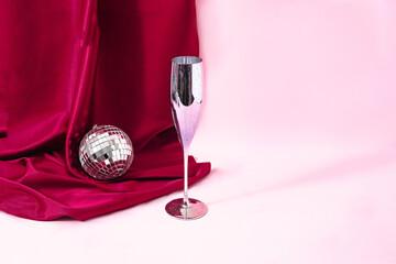 A silver Champagne glass and a shiny silver disco bauble in front of a magenta curtain against light pink background. Minimal elegant concept for Christmas or New Year celebration banner or card. 