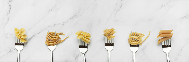 Background with forks with different pasta on a gray table