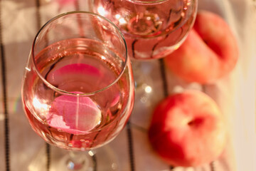 Glass of delicious rose wine with petals and peaches on white picnic blanket, closeup. Space for text