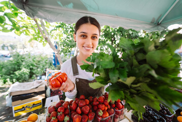 Young saleswoman at work, holding parsley and tomato in hands