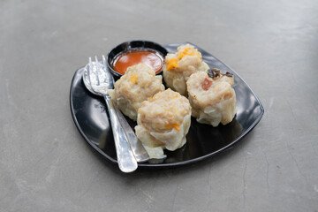 A portion of dimsum dumplings served with sambal sauce put on black plate and raw industrial background
