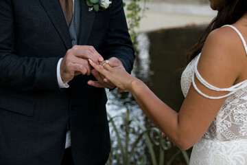 Close-up bride and groom putting an engagement ring on finger with celebrant background	