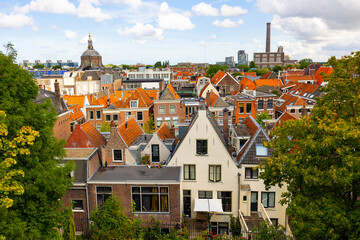 Scenic cityscape of Leiden with brownish tiled roofs of residential buildings, dome of medieval Church of St. Mary and chimney of power station at background on summer day, Netherlands..