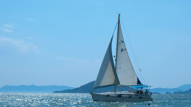 One yacht with white sail in open sea. A nice luxury yacht with sails floating on the blue waves. A concept of expensive summer relaxation on water.