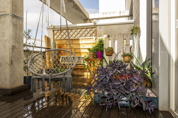 Terrace of a penthouse townhouse with acacia floors wet from the rain with a Balinese hammock between plants and pots