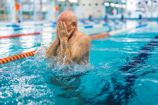 Unrecognizable bald caucasian senior adult man in a swimming pool covering his face with both hands. Leisure time activities. Active seniors. High quality photo