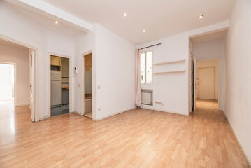 Empty living room of a house with access to several rooms, a wooden floor and narrow white aluminum windows