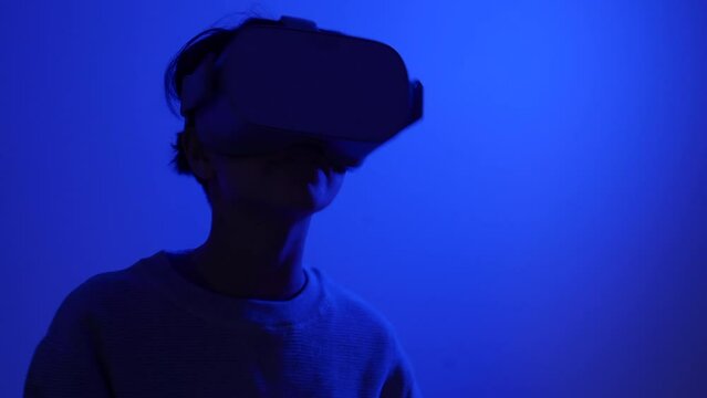 Young teenager wearing VR augmented reality goggles dancing in blue room