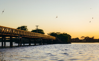 Obraz na płótnie Canvas Beautiful landscape with an old iron and wooden bridge, a river and birds flying in the sky during sunset in Colonia Carlos Pellegrini, Iberá Wetland Provincial Nature Reserve, Corrientes, Argentina.