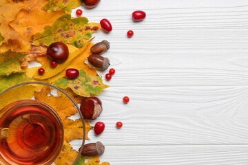 Naklejka na ściany i meble Different autumn leaves, acorns, chestnuts, red berries and cup of tasty tea on white wooden table, flat lay. Space for text