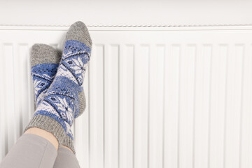 Woman warming feet near heating radiator, closeup. Space for text