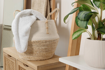 Wicker basket with white soft towel on wooden stand in bathroom
