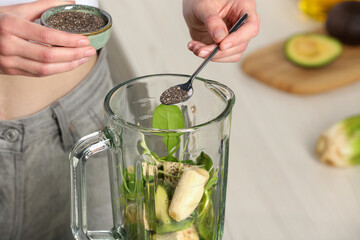 Woman adding chia seeds into blender with ingredients for green smoothie, closeup