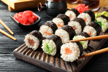 Set of delicious sushi rolls and chopsticks on black wooden table, closeup