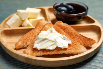 Tasty toasts with butter and blueberry jam on light blue wooden table, closeup