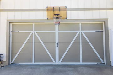 A basketball hoop mounted outside and above the garage of a new construction cream colored house - Powered by Adobe
