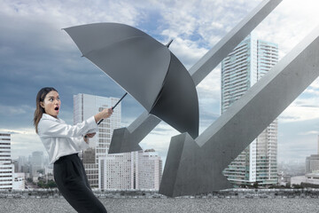 Asian businesswoman tries to hold back a falling arrow with a black umbrella