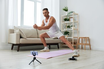 Fototapeta na wymiar Man sports, watching a workout tape on his phone and repeating exercises blogger, pumped up man fitness trainer works out at home, the concept of health and body beauty