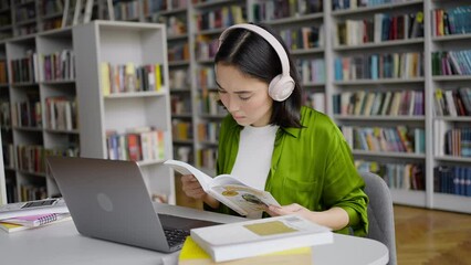 Young Asian woman in headphones types on laptop in library