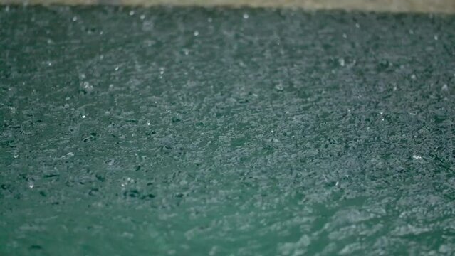 Tropical rain drops falling onto the surface of a swimming pool. Slow motion