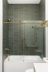 A shower with green subway tiles, gold faucet and accents, and a white bathtub.