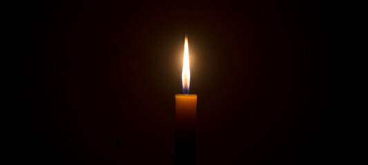 A single burning candle flame or light glowing on a white candle on black or dark background on...