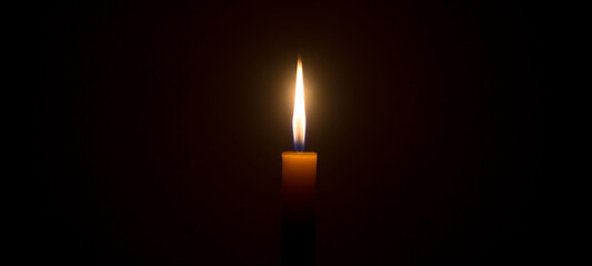 A single burning candle flame or light glowing on a white candle on black or dark background on...
