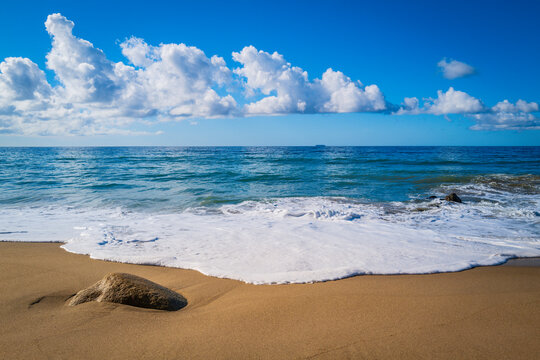 Tranquil Zen-like seascape of Zuma Beach, Malibu, California, with white rocks, waves rolling in on the clean sand, and white clouds over the blue horizon