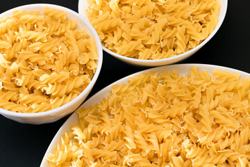 Uncooked Fusilli Pasta Lying on White Plate on Black Background. Raw and Dry Macaroni. Unhealthy and Fat Food