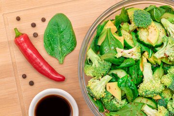 Fresh Green Salad of Avocado, Broccoli, Spinach and Cucumber with Soy Sauce and Red Hot Pepper on Wooden Cutting Board. Vegan Salad. Vegetarian Culture. Raw Food. Healthy Eating and Vegetable Diet