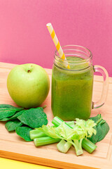 Fresh Green Smoothie of Apple, Celery, and Spinach in Glass Smoothie Jar with Yellow Cocktail Straw on Wooden Cutting Board. Vegan Detox Drink. Vegetarian Culture. Healthy Eating and Fruit Diet