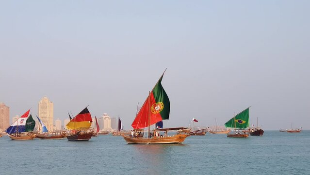 Sailing traditional lenj boat ship with country flag sail like potugal brazil serbia germany football team in the sea with doha towers cityscape in qatar during fifa world cup 2022 near the beach