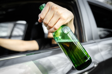 Close-up of a bottle of beer in the driver hand in window car. Alcohol driving concept.