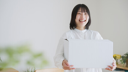笑顔でダンボールを持つ女性（引越し・通販）..