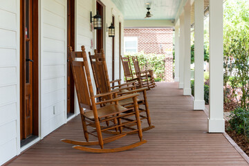 Multiple vintage brown wooden rocking chairs on the veranda of an old white colored country house...
