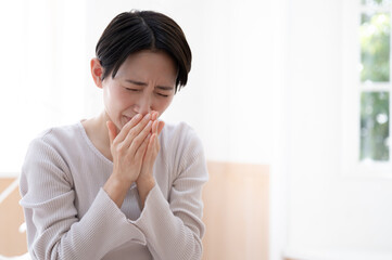 くしゃみをして風邪気味な女性 右にコピースペースあり