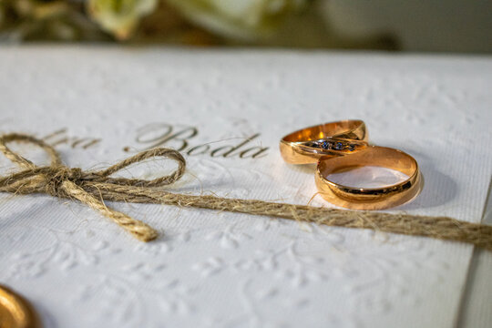 Engagement rings on top of a wedding invitation with a gold seal next to a bouquet of flowers