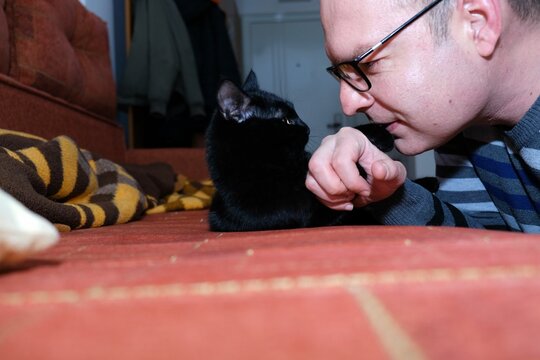 Caucasian Man Playing With A Black Cat At Home