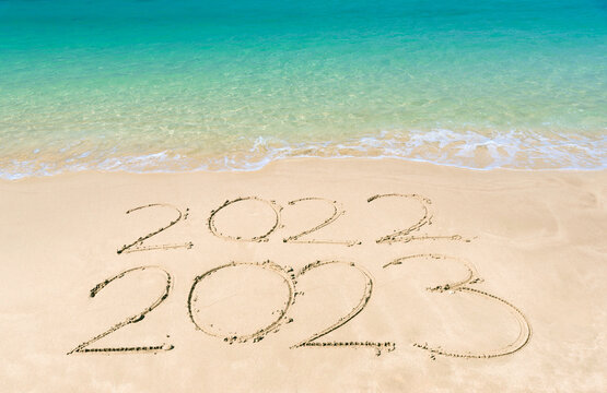 End of 2022 Happy New Year 2023, lettering on sunrise beach with wave and foam bubble in the morning. Handwritten inscription 2022 and 2023 on beautiful sand beach. New Year 2023 replace 2022 concept.