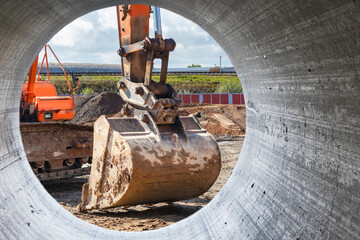 Excavator bucket close-up view from a large diameter pipe. Heavy earthmoving equipment. Soil development. Laying of underground communications. Construction machinery and equipment.
