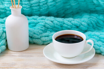 Cup of hot coffee, aroma reed diffuser and a turquoise blanket