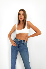 Young model woman in white underwear and jeans posing on studio background
