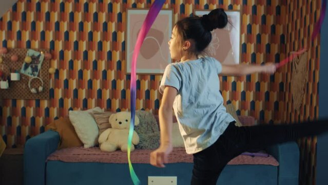 Young asian schoolgirl dances with gymnastic ribbon, showing vertical leg-split and spins around herself. Rhythmic gymnastics. Sports hobby. Upgrading physical health on quarantine. Slow motion.