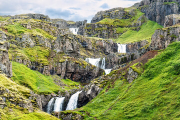 Klifbrekkufossar multi tiered waterfall flowing from cliff amongst green moss in Mjoifjordur fjord...