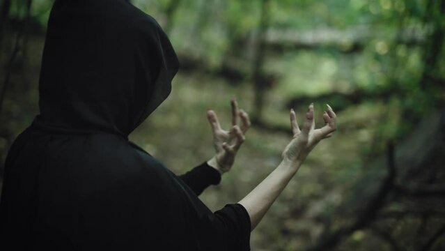 A mysterious black hooded figure practices witchcraft and black magic in a mysterious forest. A witch from the piercing, causes ancient curses.
