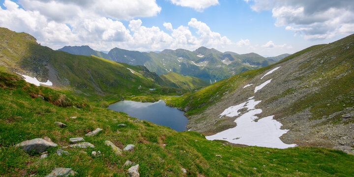 high altitude mountain lake. beautiful nature landscape of romania. grass and snow on the hills. sunny weather with clouds on the sky in summer