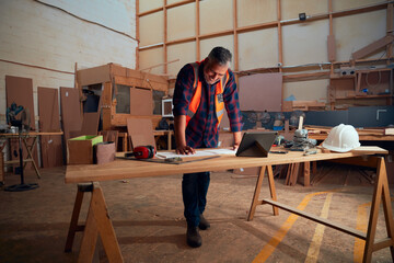 Mid adult man working next to digital tablet and tools on table in woodworking factory